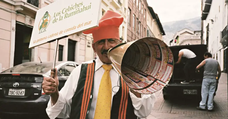 A street performer in Quito, Ecuador, promoting Los Cebiches de la Rumiñahui with a sign and megaphone.