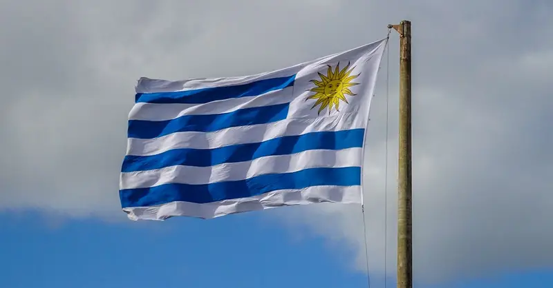 The national flag of Uruguay waves on a flagpole against a bright cloudy sky in Punta del Este.