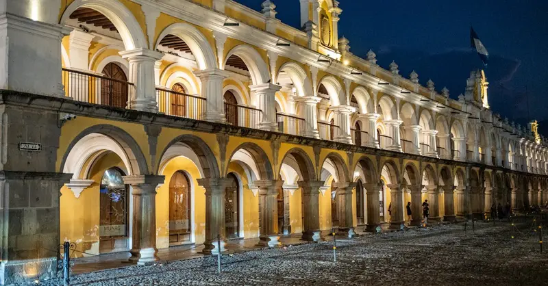 Night view of the illuminated colonial building Arco de Santa Catalina in Antigua Guatemala, showcasing vibrant arches.