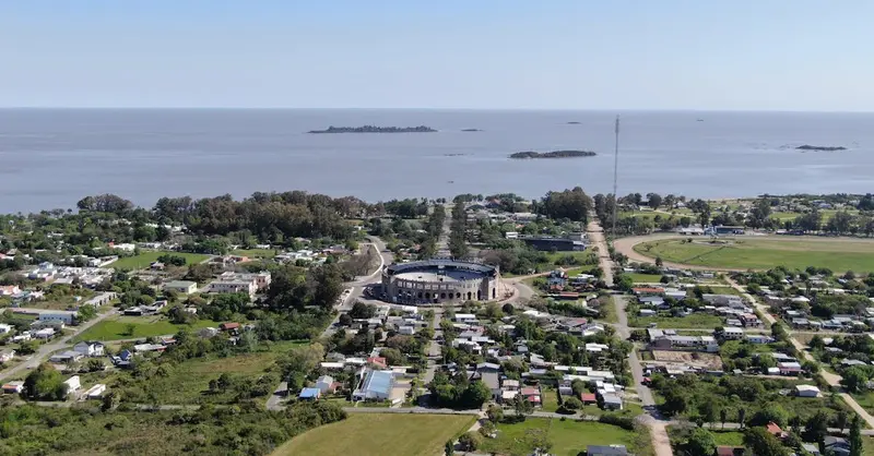 Aerial view of Colonia Del Sacramento, featuring the coast and Plaza de Toros with lush greenery.