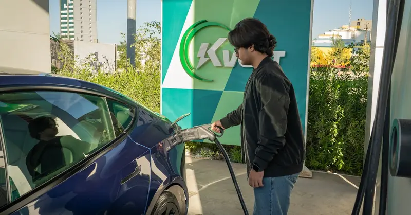Young man charging a Tesla Model 3 at an outdoor electric vehicle station during the day.