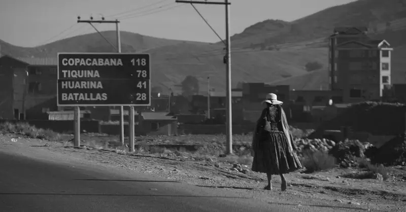A woman in traditional dress walks a road in El Alto. Sign shows directions to Bolivian destinations.