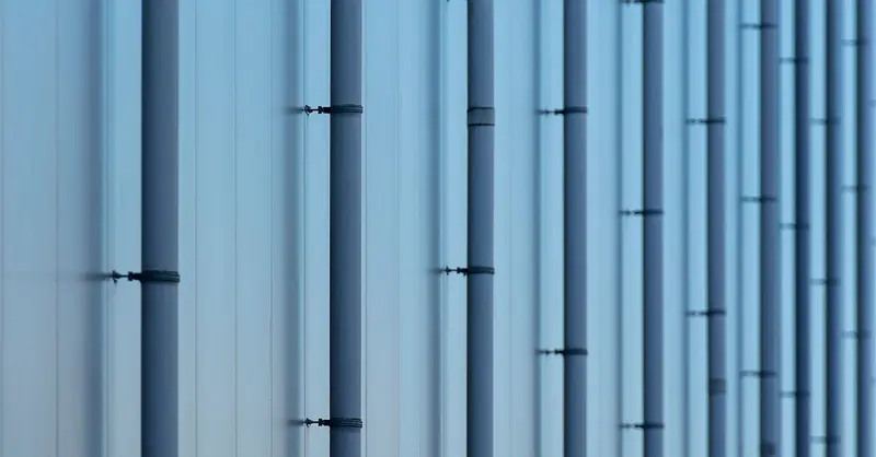 Close-up of blue metal pipes on the exterior of an industrial building, creating a symmetrical pattern.