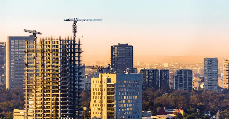 Aerial view of construction cranes and skyscrapers in Ciudad de México at sunset.