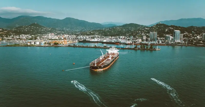 Stunning aerial view of a large ship in the port of Batumi, Georgia, surrounded by lush mountains.