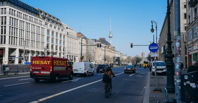 Berlin street view featuring a cyclist and iconic TV Tower under a clear blue sky.