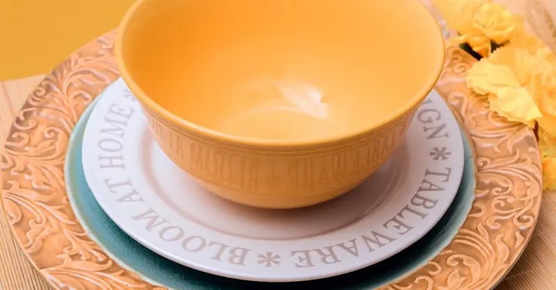 Artistic presentation of a yellow ceramic bowl set on a detailed decorative plate with autumnal floral accents.