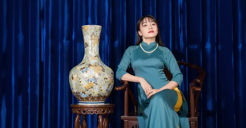 An elegant woman poses in a traditional Vietnamese dress next to a decorative ceramic vase.