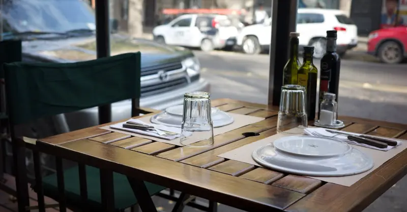An outdoor dining setup in a Mendoza restaurant with wine bottles and plates.