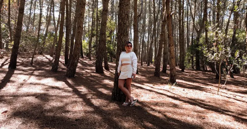A woman stands in a sunlit pine forest in Mar de las Pampas, Argentina.