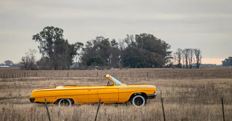 Vintage yellow convertible in a serene rural field in Coronel Pringles, Argentina, evoking nostalgia in an open landscape.
