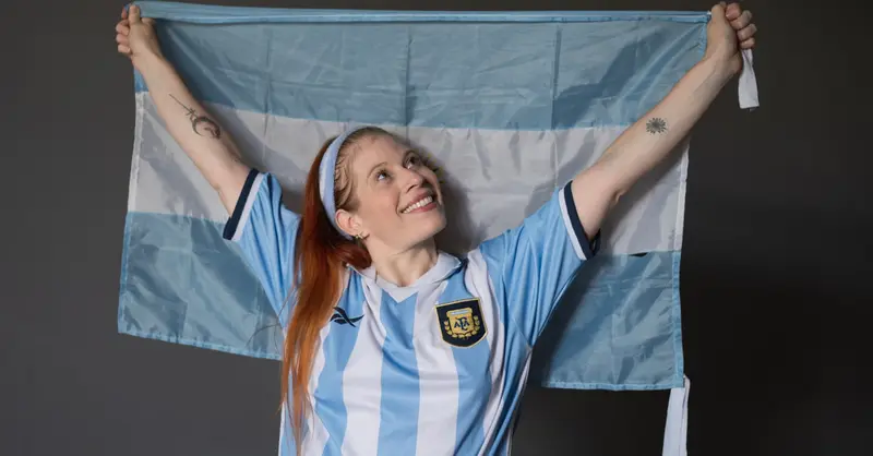 Joyful woman holding Argentina flag wearing national jersey indoors.