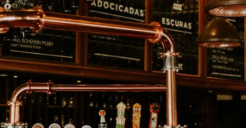 Close-up of a brewery taproom interior featuring copper pipes and beer taps. Ideal for beverage industry visuals.
