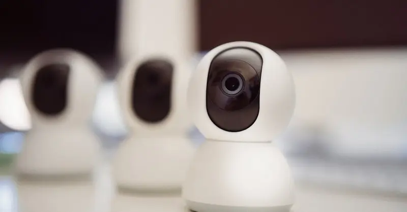 Close-up of three smart home security cameras placed on a white desk indoors.