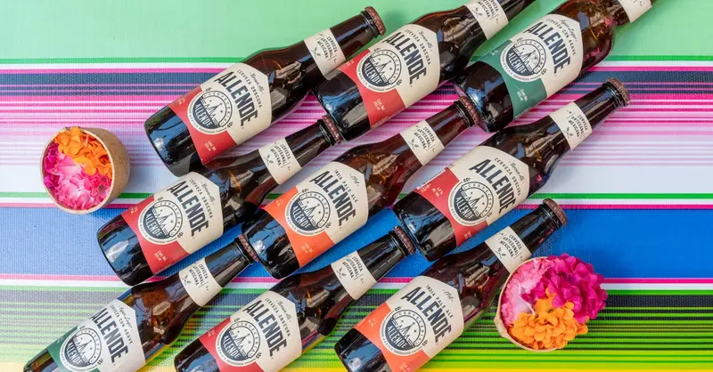 Top view of Mexican craft beer bottles on a striped, colorful background with flower decorations.