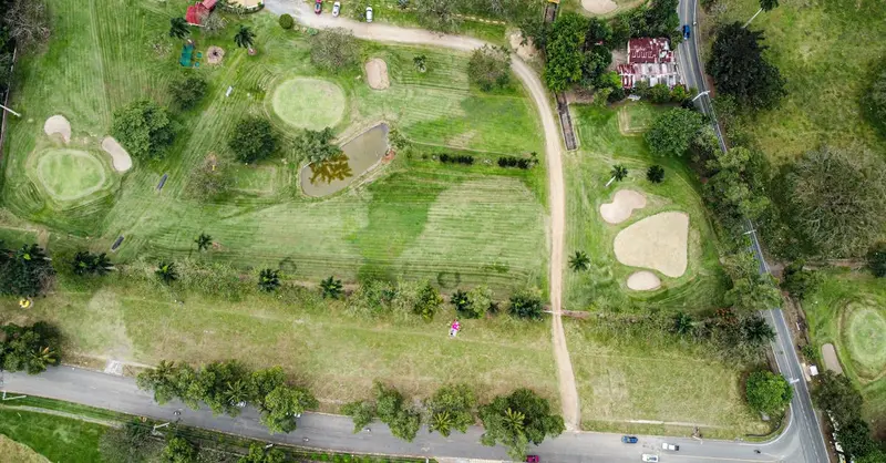 High-angle aerial shot capturing a verdant golf course with distinct greens, bunkers, and paths surrounded by lush trees.