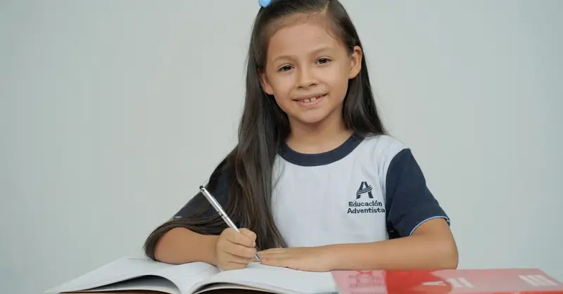A young girl sitting at a desk, studying with open books and smiling.