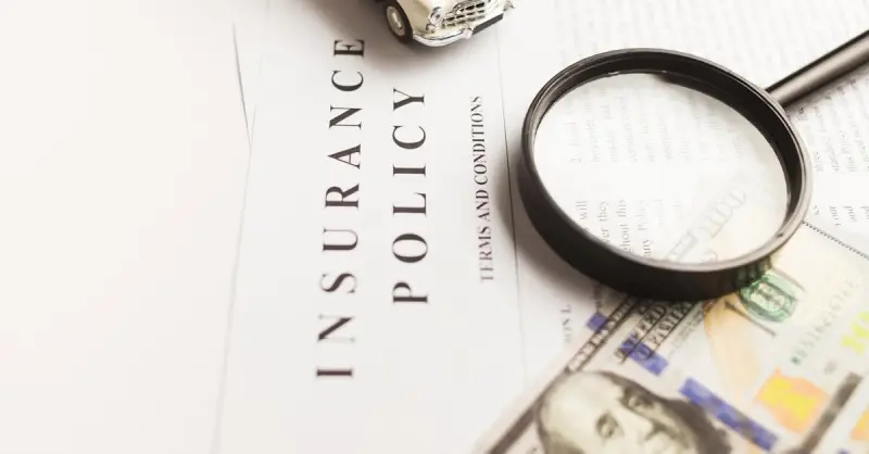 Close-up image of an insurance policy with a magnifying glass, money, and toy car.