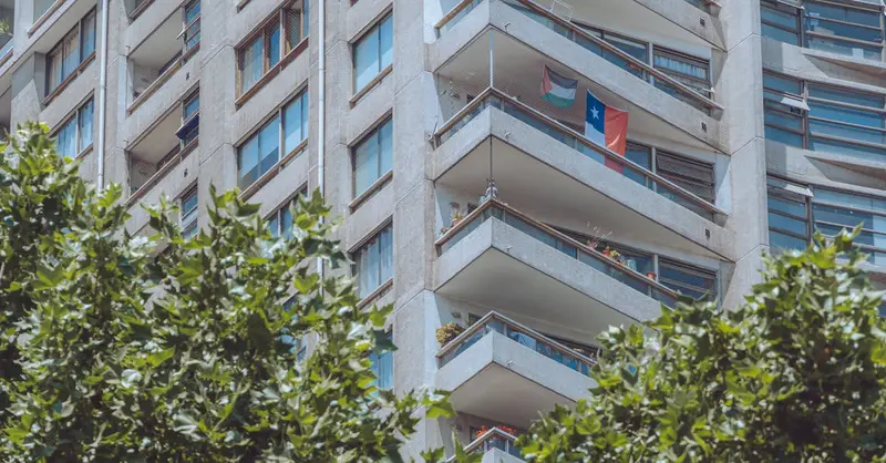 Modern apartment building in Santiago with a Chilean flag on the balcony, surrounded by greenery.