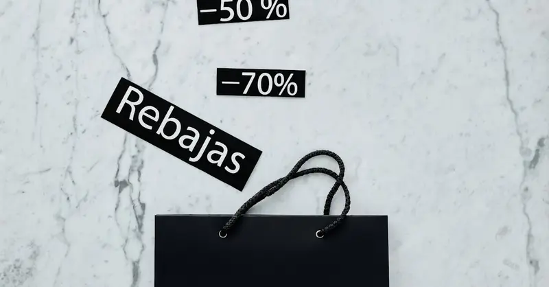 Modern flat lay featuring a black shopping bag with 50% and 70% sale tags on a marble surface.