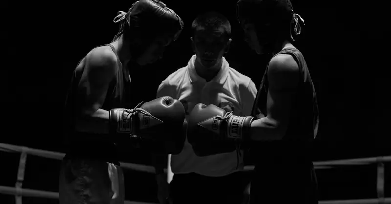 Two boxers face off in a dimly lit ring under a referee's watchful eye in Lautaro, Chile.
