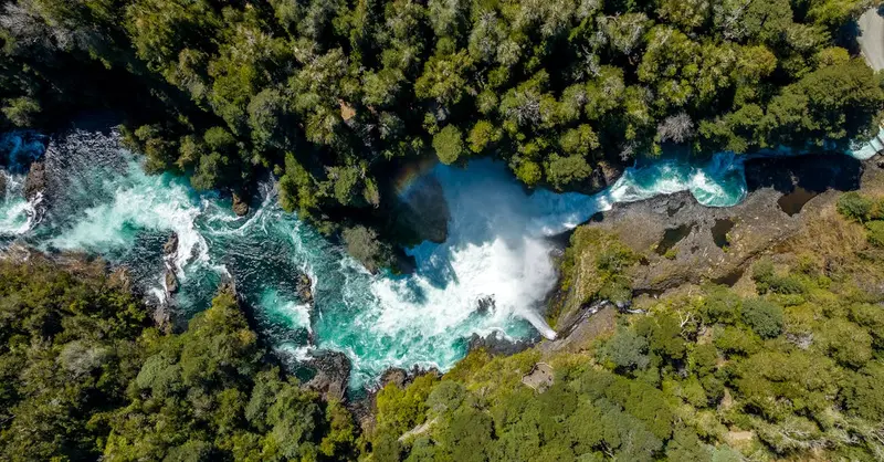 Stunning aerial view of a turquoise waterfall cascading through lush forest in Panguipulli, Chile.