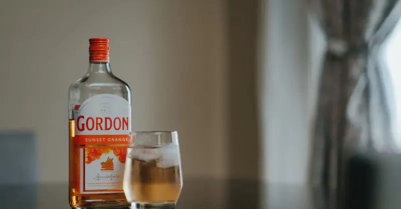 Close-up of Gordon's Sunset Orange gin bottle and glass with ice indoors.