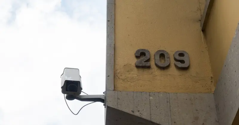 Close-up view of a yellow building corner with a security camera and address number 209 in Toluca, Mexico.