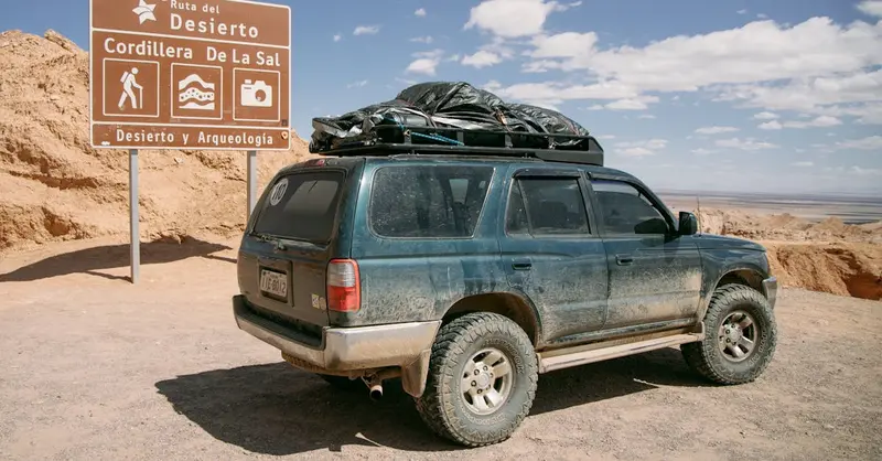 A dusty SUV parked near a sign in Cordillera de la Sal, Chile's Atacama Desert.