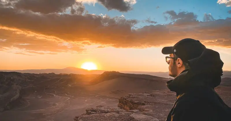 Man enjoys a stunning sunset view over a vast desert landscape, capturing tranquility.