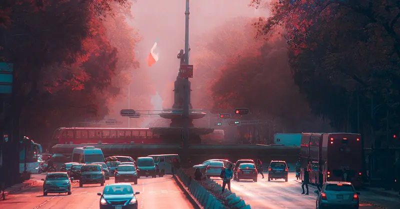 Evening traffic on Paseo de la Reforma in Mexico City with vibrant lighting and the Mexican flag in view.