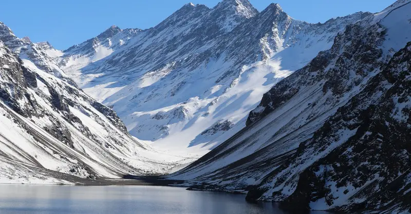 A breathtaking view of the snow-covered Andes mountains and a serene lake in Chile during winter.