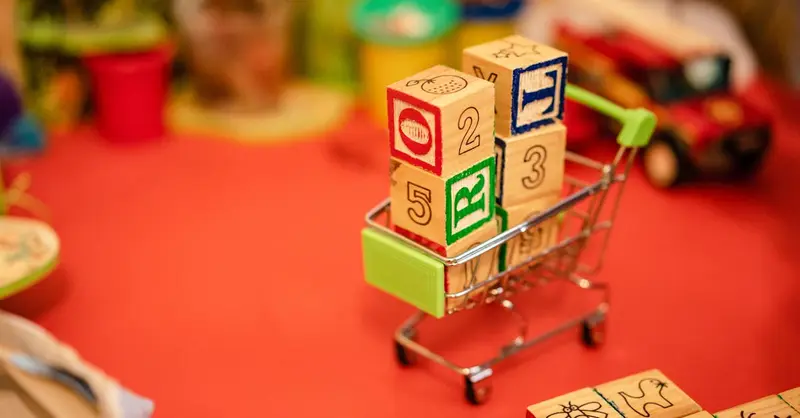 Miniature shopping cart filled with vibrant wooden blocks on a playful background.