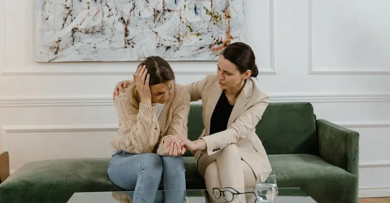 A therapy session where a concerned therapist supports a distressed woman in a modern office.