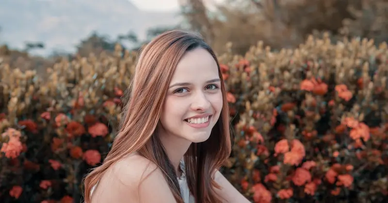 A young woman smiling in front of vibrant orange flowers with mountains in the background.