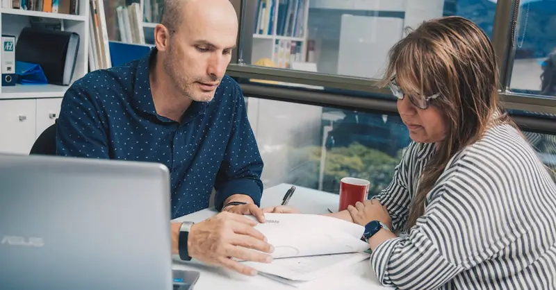 Coworkers working together with documents while sitting at table with laptop near window in modern light office
