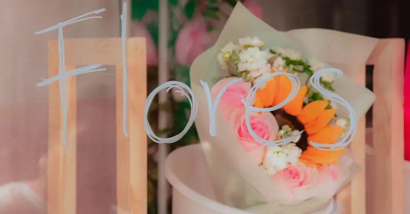 A vibrant bouquet of flowers behind a glass with 'Flores' written on it, softly lit.