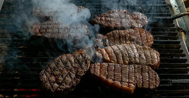 Juicy beef steaks being grilled with smoke rising, perfect for barbecue enthusiasts.