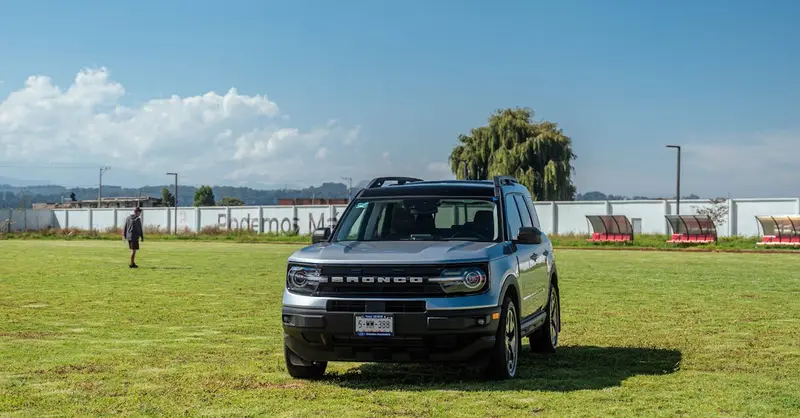 A silver Ford Bronco park on a grassy field under a blue sky, showcasing a rural landscape.