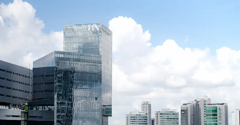 Panoramic view of sleek, glass skyscrapers with blue sky and clouds.