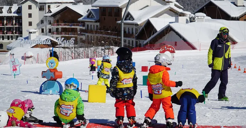 Kids in colorful outfits enjoying ski lessons on a snowy slope in Adlerskiy, Russia.
