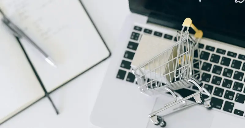 Creative depiction of online shopping with a miniature cart on a laptop keyboard.