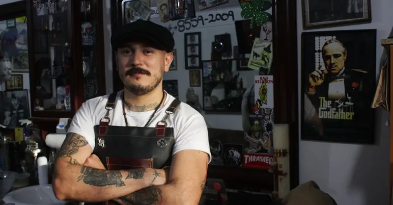 Portrait of a tattooed barber standing confidently in a vintage-style barber shop.