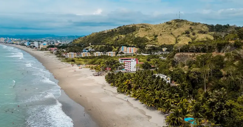 Scenic aerial view of a coastal town with tropical beach and lush hills.