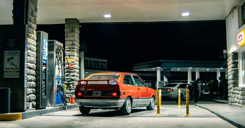 A classic red Volkswagen refuels at a rustic gas station in El Bolsón, Argentina.