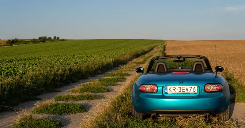 Convertible Mazda MX-5 on a picturesque rural road in Poland's countryside.