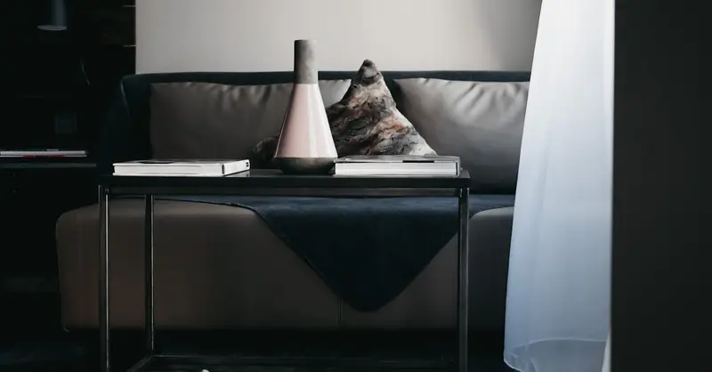 Stylish vase and books arranged on table placed near comfortable leather couch in modern apartment