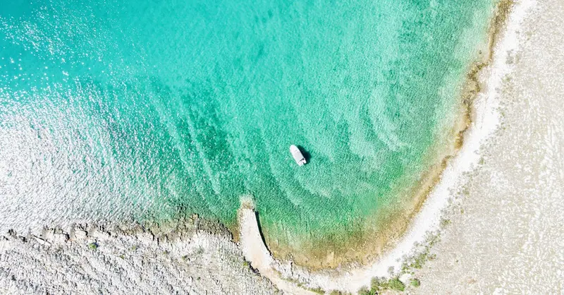 A breathtaking aerial view of a serene Croatian beach with crystal clear waters and a lone boat.