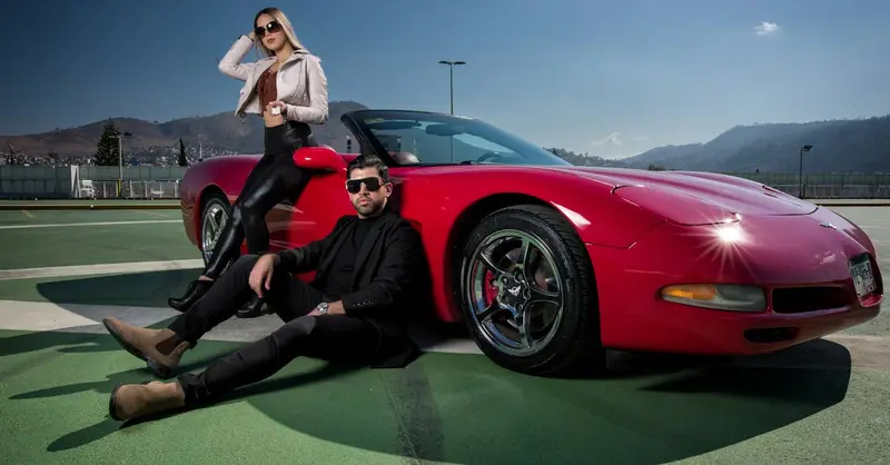 A fashionable couple posing confidently with a red convertible sports car outdoors.