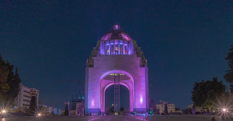 Vibrant night view of Monumento a la Revolución with purple lighting in Mexico City.